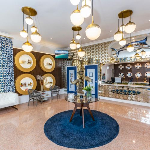 A stylish hotel lobby with art deco decor, blue accents, and a nautical theme, featuring a marlin sculpture and round shelved walls.