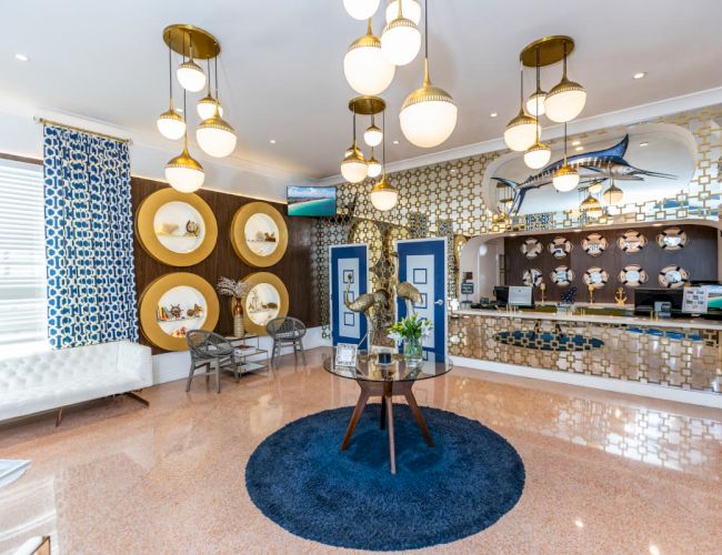 A stylish hotel lobby with art deco decor, blue accents, and a nautical theme, featuring a marlin sculpture and round shelved walls.