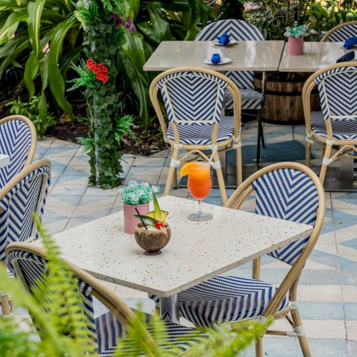 Outdoor cafe with blue-striped chairs, plants, and a table with a coconut drink and an orange cocktail.