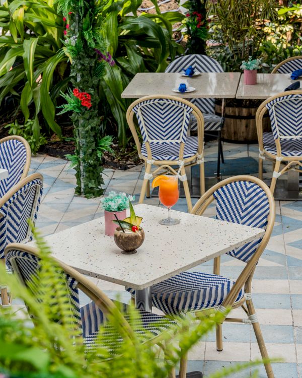 Outdoor cafe with blue-striped chairs, plants, and a table with a coconut drink and an orange cocktail.