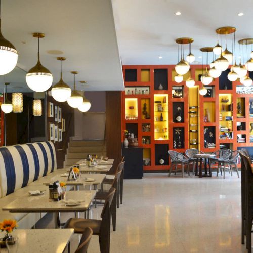 A modern restaurant interior with striped seating, hanging lights, and colorful shelves filled with decor and books on the walls.