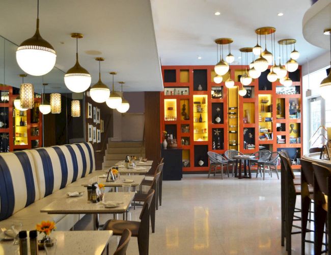 A modern restaurant interior with striped seating, hanging lights, and colorful shelves filled with decor and books on the walls.