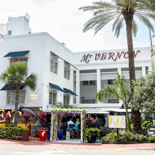 The image shows a white building with "Mt Vernon" signage, surrounded by palm trees and a landscaped garden.