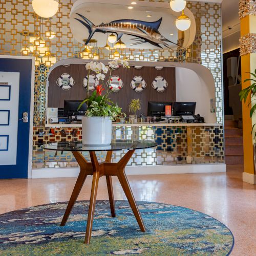 A hotel lobby with a nautical theme, featuring floral arrangements, bold blue doors, a marlin sculpture, and decorative light fixtures.