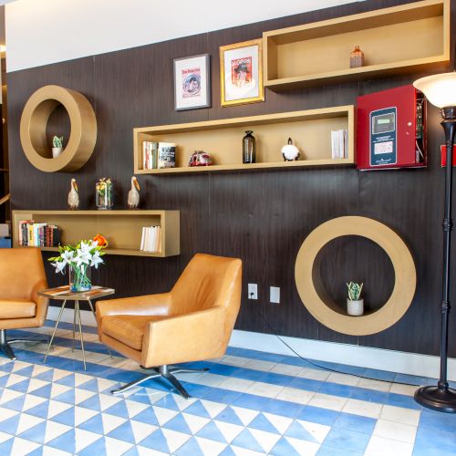 A modern lounge area with two leather chairs, wall shelves, framed pictures, and stylish decor accents.