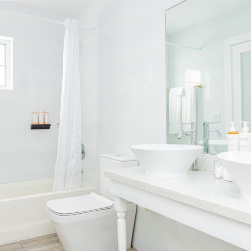 A modern bathroom features twin sinks, a mirror, a bathtub with a curtain, white walls, and toiletries on the counter.
