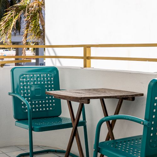 A small patio with two teal chairs and a wooden table, surrounded by a yellow railing.