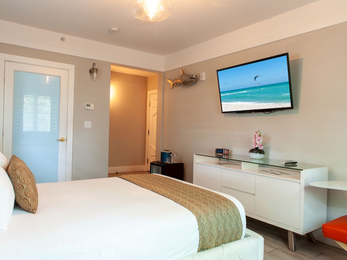 A modern bedroom with a bed, TV, decorative lamp, and a vase on a dresser. The TV displays a beach scene, adding a relaxing vibe.