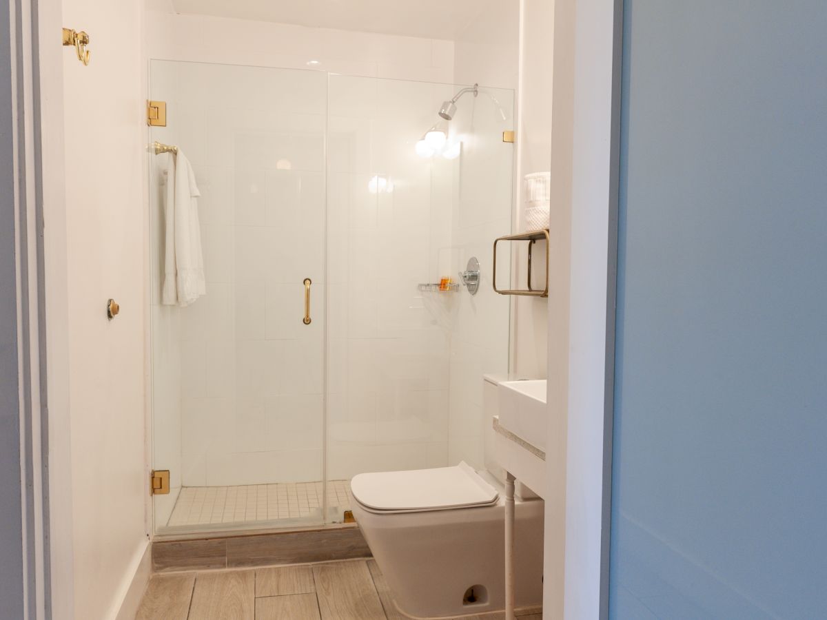 A modern bathroom with a glass shower, white sink, toilet, and towel hung near gold hardware ends the sentence.