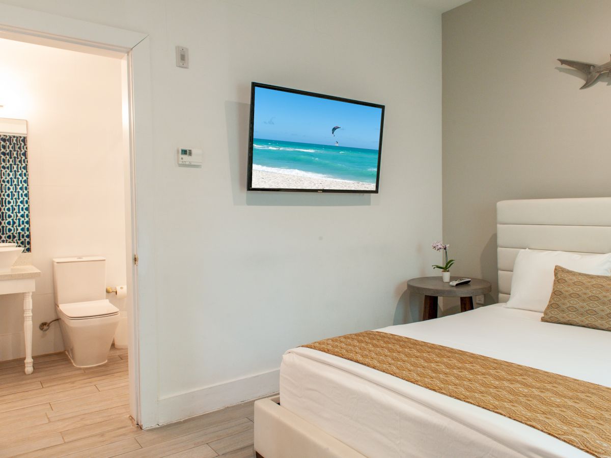 A modern hotel room with a bed, wall-mounted TV, bathroom, and ocean decor.