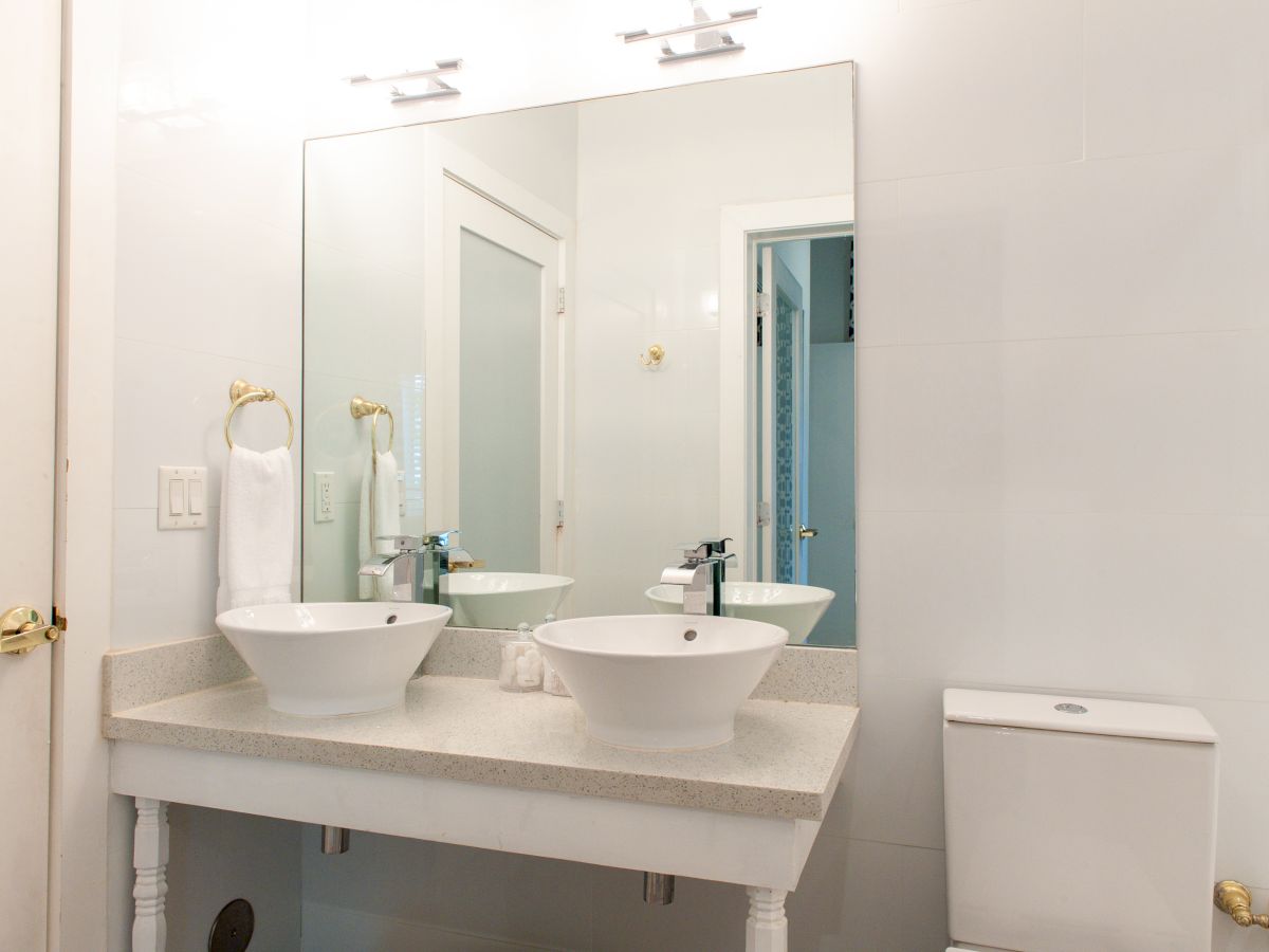 A bright bathroom with twin vessel sinks, large mirror, toilet, towel, and modern fixtures.