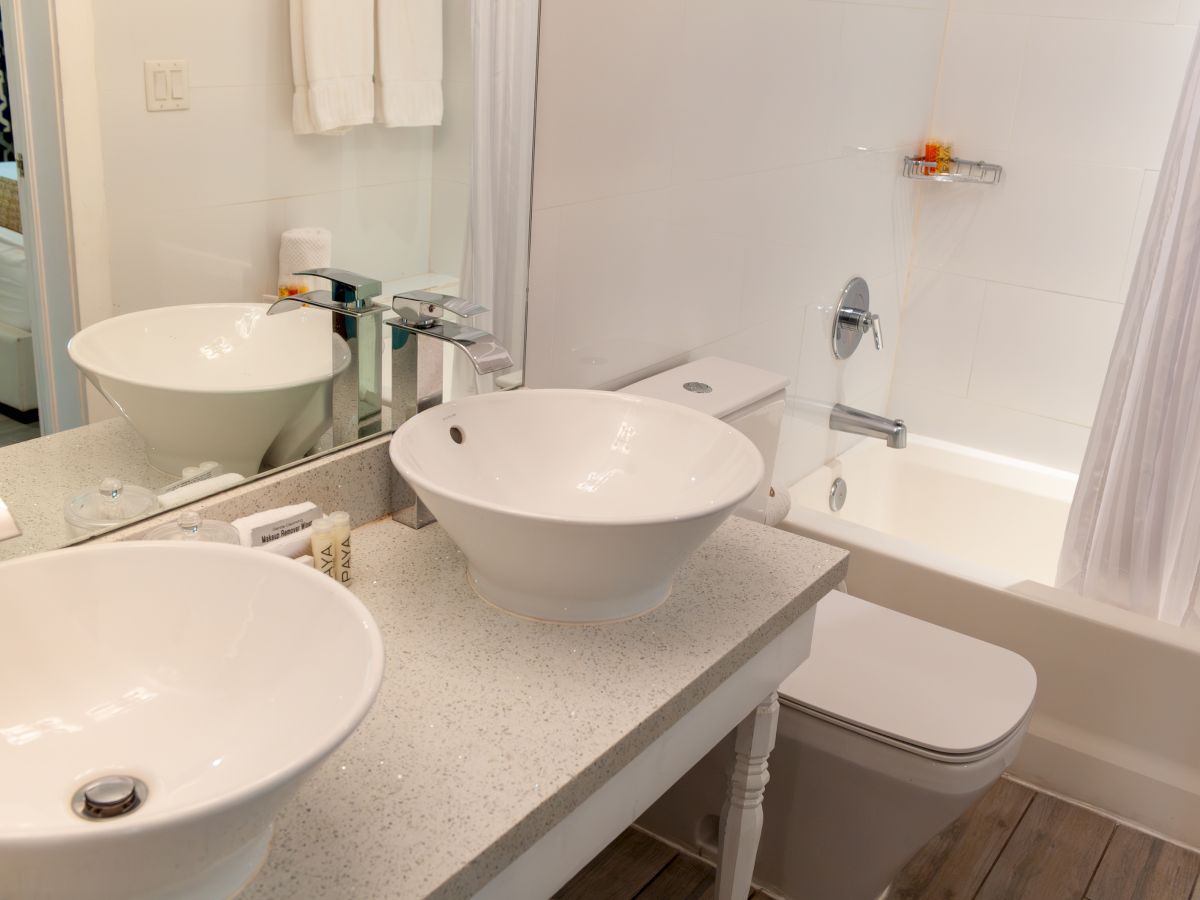 A modern bathroom with double sinks, a toilet, and a bathtub. Towels and toiletries are neatly arranged on the countertop.