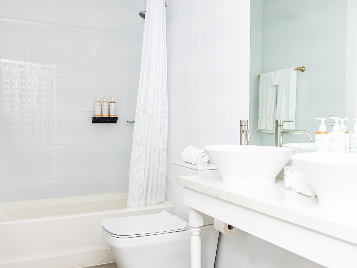 A clean, white bathroom with a tub, shower curtain, sink with soap dispensers, towels, and a toilet.
