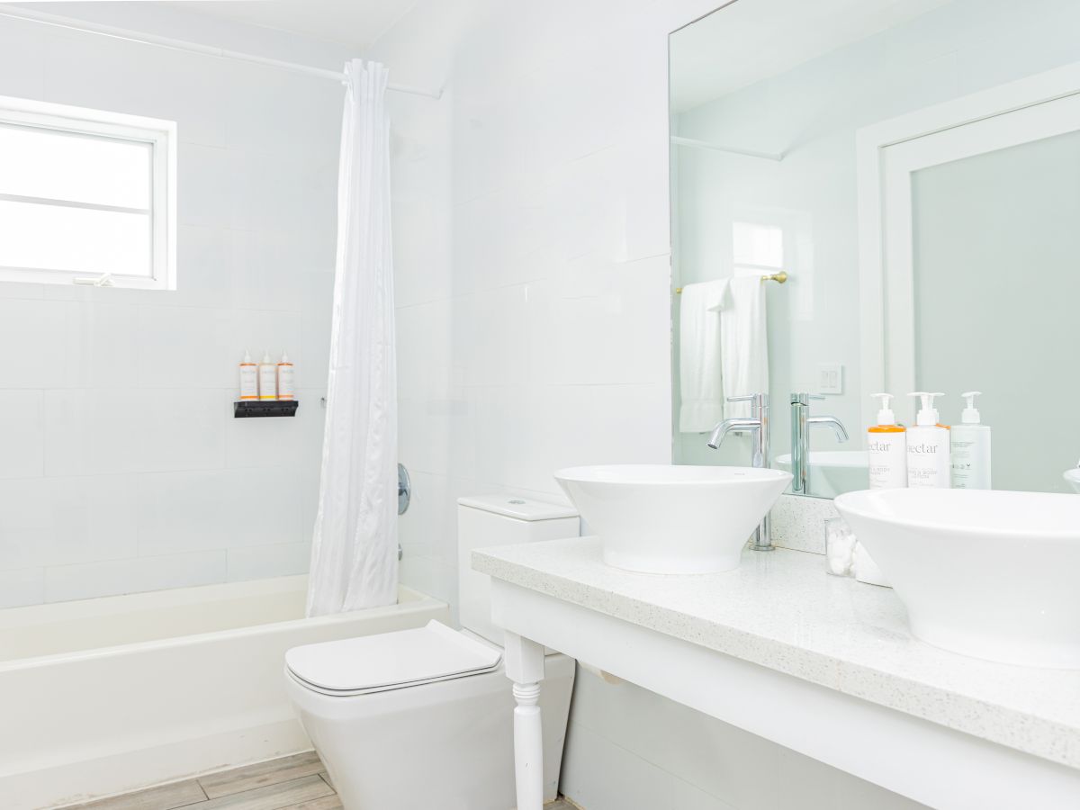 A bright bathroom with a bathtub, shower curtain, toilet, double sink, mirror, and toiletries on the countertop.