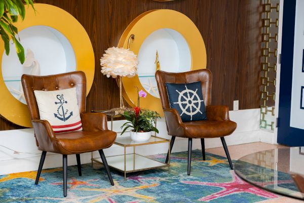 A stylish room with two brown chairs, nautical-themed cushions, a decorative plant, and round wall features on a colorful rug.