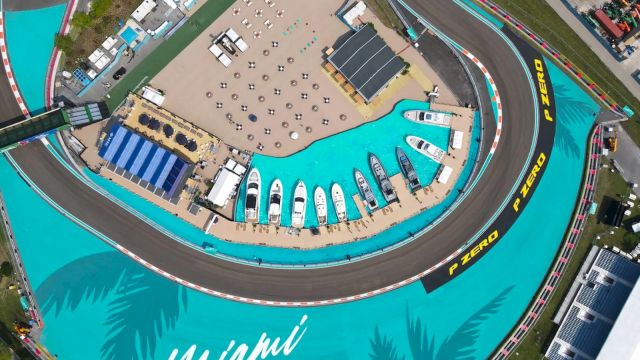 Aerial view of a race track with yachts docked nearby, surrounded by teal blue areas, marked "Miami" and "P Zero" on the track.