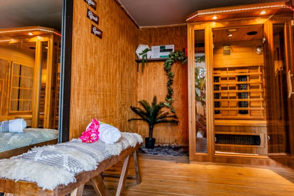This image shows a cozy spa room with a wooden sauna, towels on a bench, and decorative plants, creating a relaxing atmosphere.