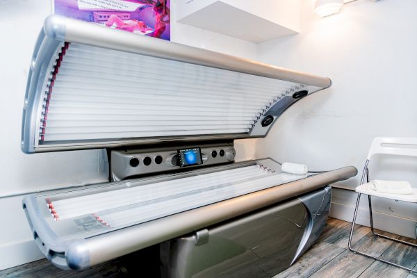 A tanning bed is open in a room with a chair and folded towels nearby.