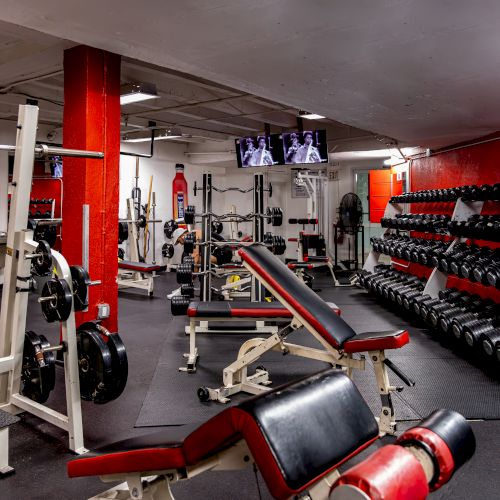 A gym with weights, benches, and equipment, featuring red accents and TVs on the wall.